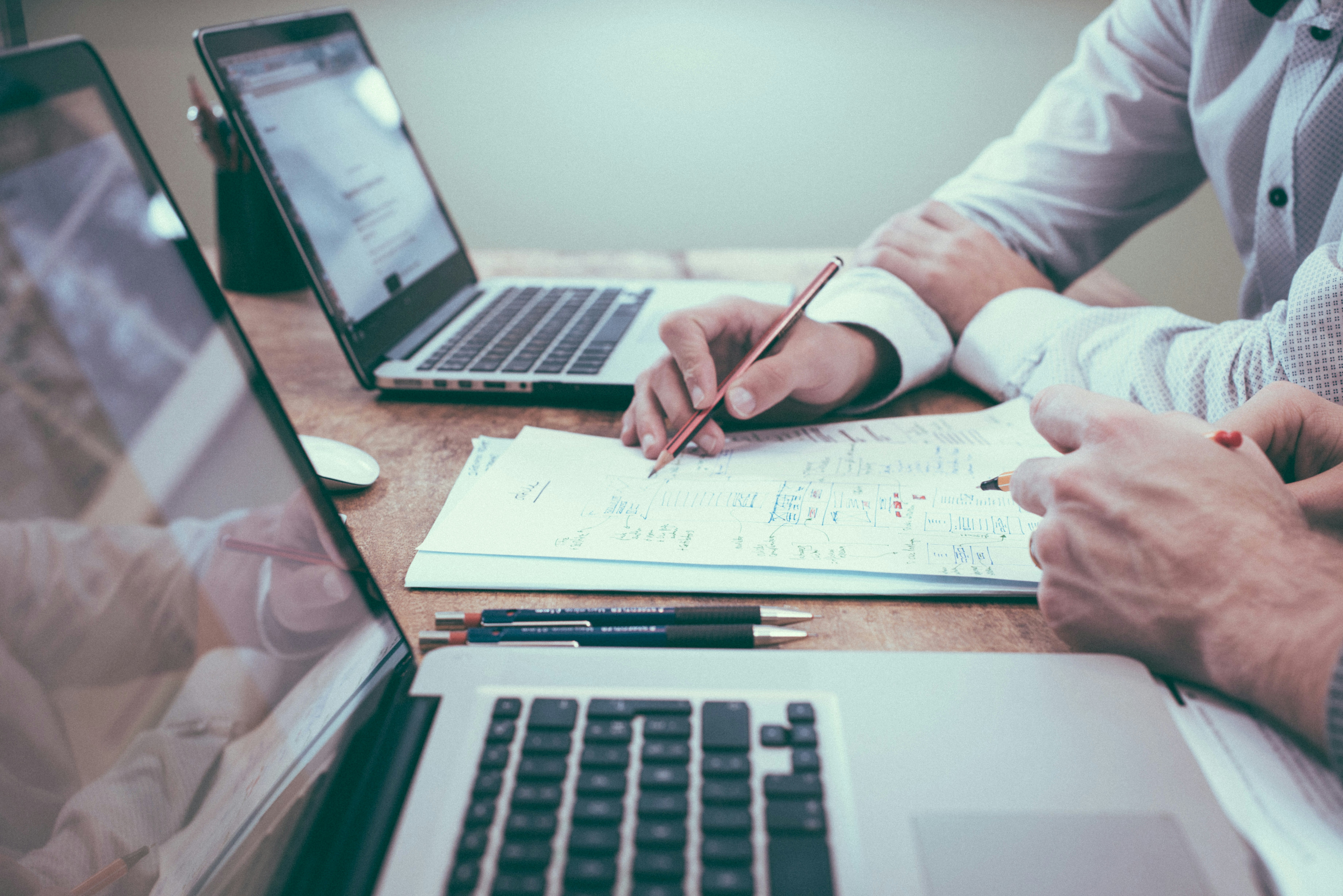 two people sitting at a table in front of laptops with papers in between that they're both reviewing | Asking for Help: Coaching for Physicians
